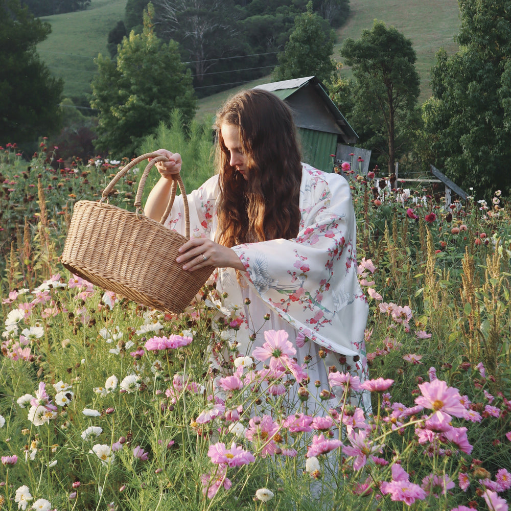 Woman in a floral dress holding a woven basket in a field of flowers with mountains in the background