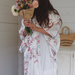 Woman in a floral kimono robe holding flowers in a room with a white wall and wooden cabinet.