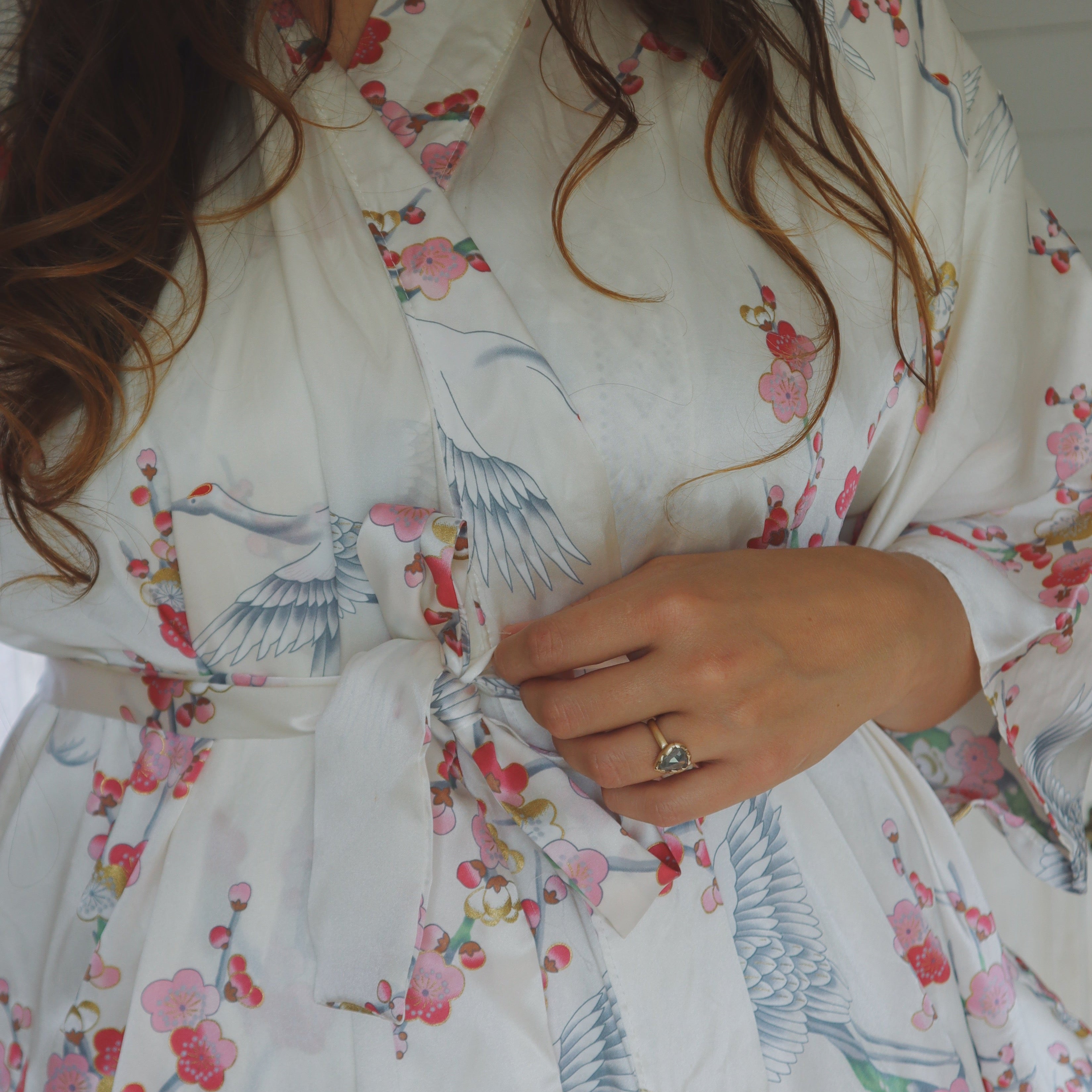 Person wearing a floral kimono robe with cranes and flowers, holding the waist.