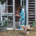 Woman in a floral kimono standing in front of a wooden shed with flowers around her.
