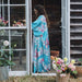 Woman in a floral dress standing in an open wooden door with flowers around her.