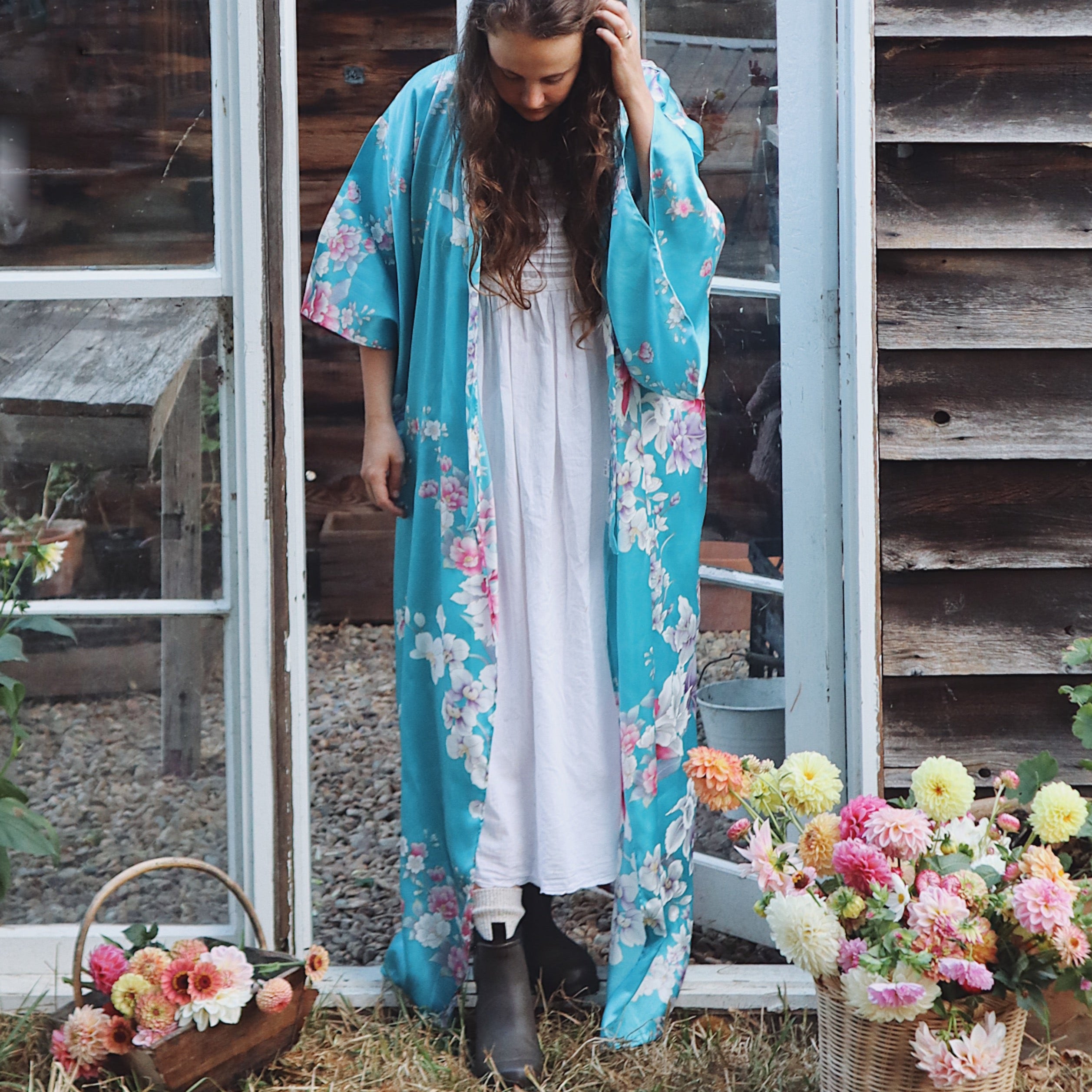 Woman wearing a floral kimono standing outdoors with flowers and a wooden door in the background