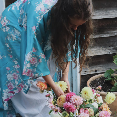 Woman in a floral kimono arranging flowers in a basket outdoors.