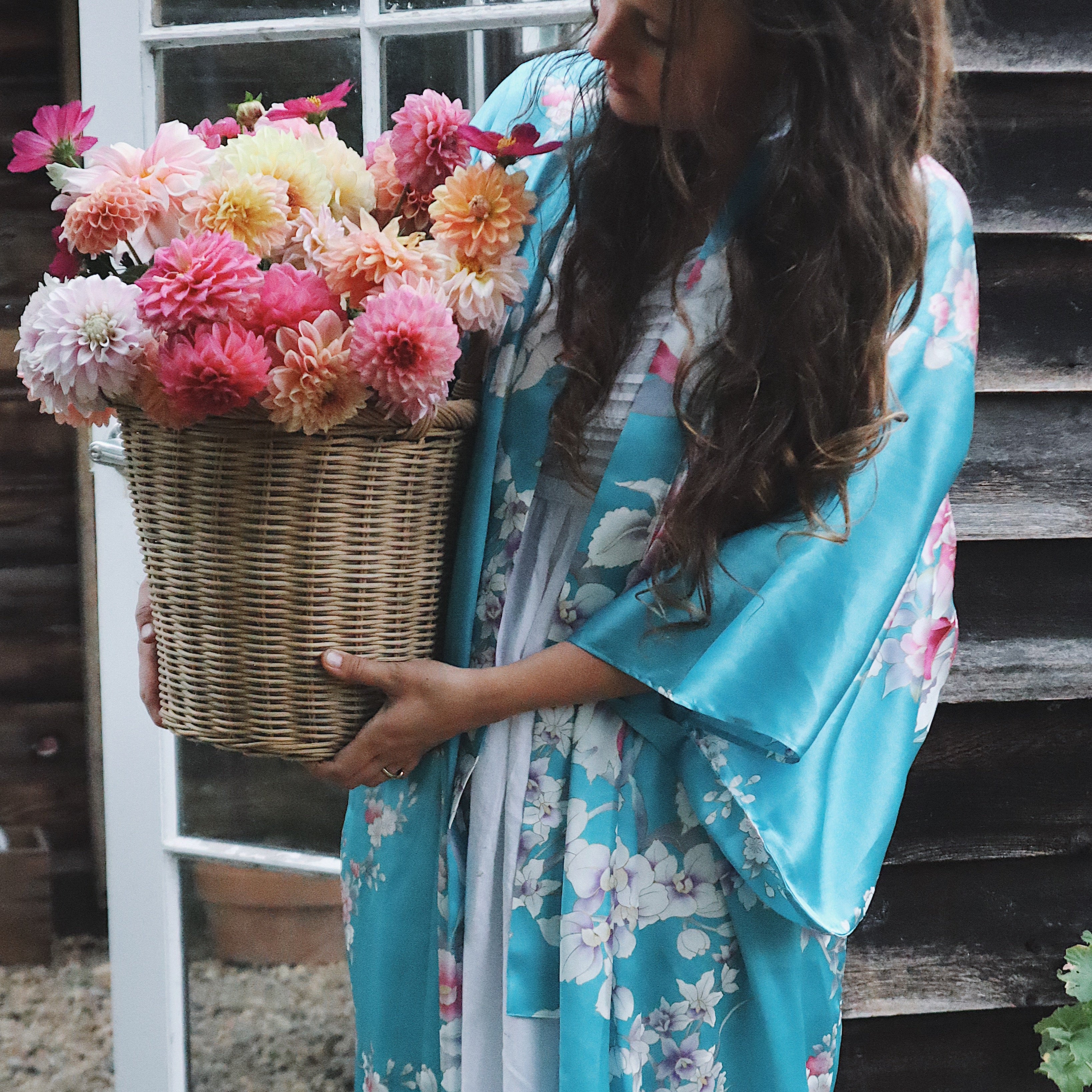 Woman in a floral kimono holding a basket of flowers in front of a wooden door.