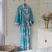 Turquoise floral kimono hanging on a hook in a room with a white dresser and decorative items.