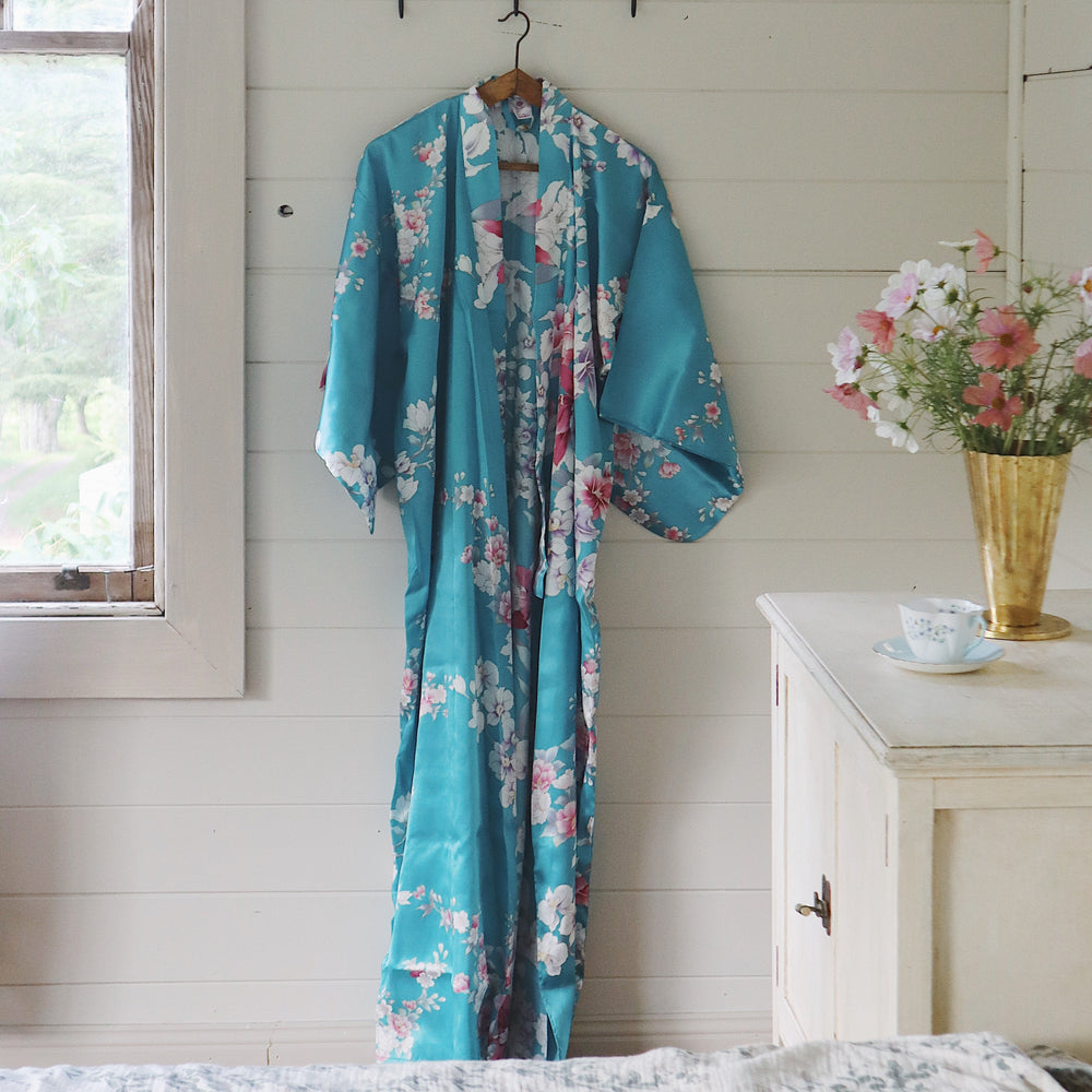 Turquoise floral kimono hanging on a hook in a room with a window and dresser.
