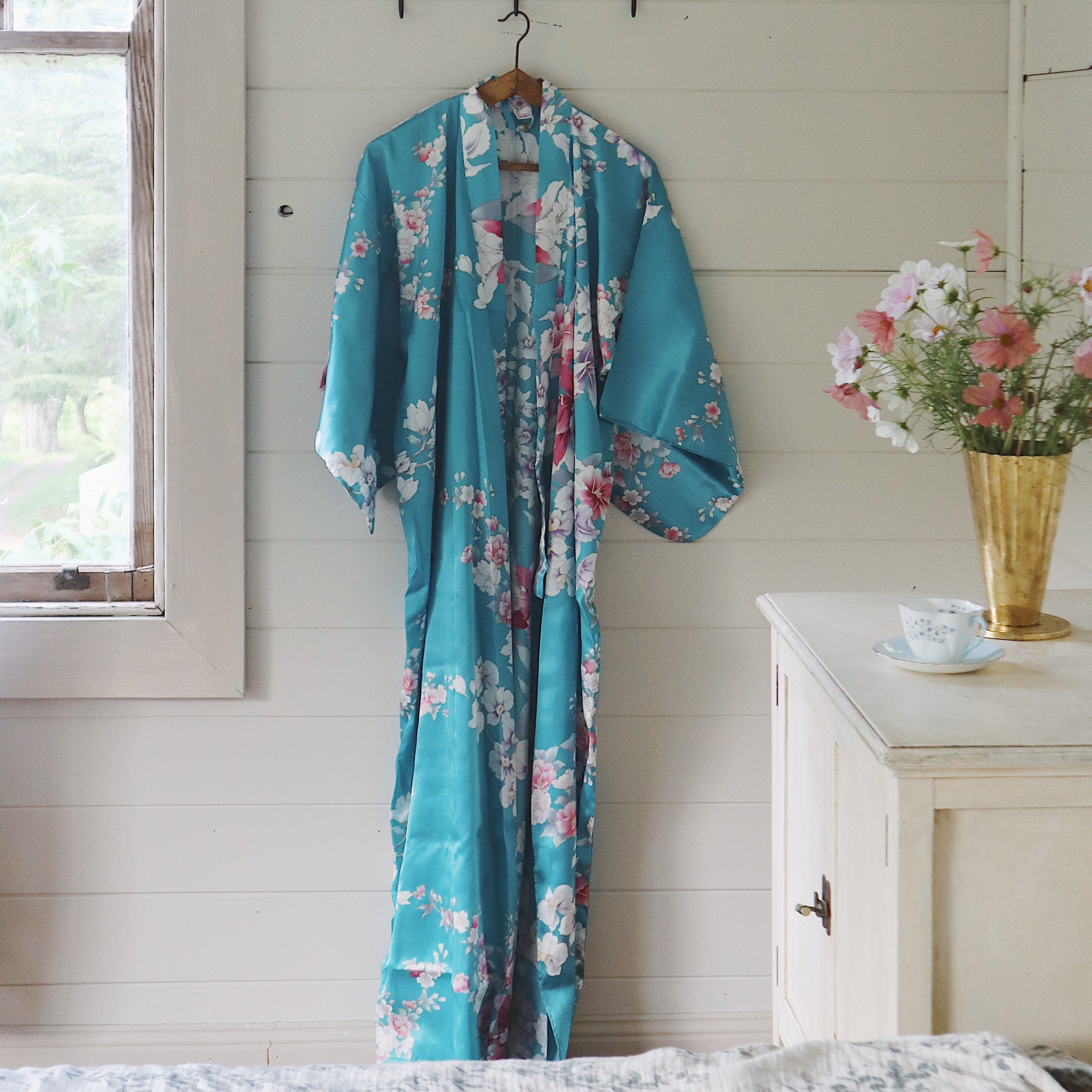 Turquoise floral kimono hanging on a hook in a room with a window and dresser.