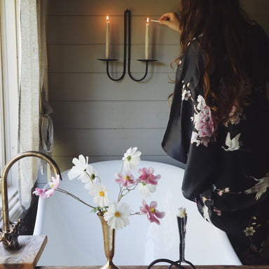 Woman in a silk kimono robe lighting a candle with flowers in a vase over a bath in the foreground