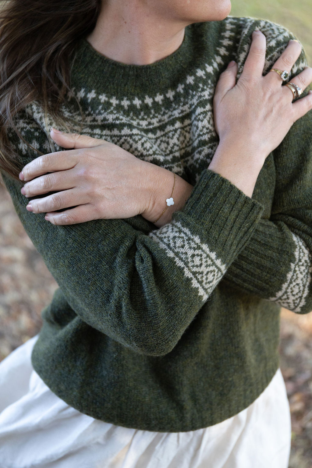 Person wearing a green fair isle knit sweater with a patterned design, holding their hands close to their chest.