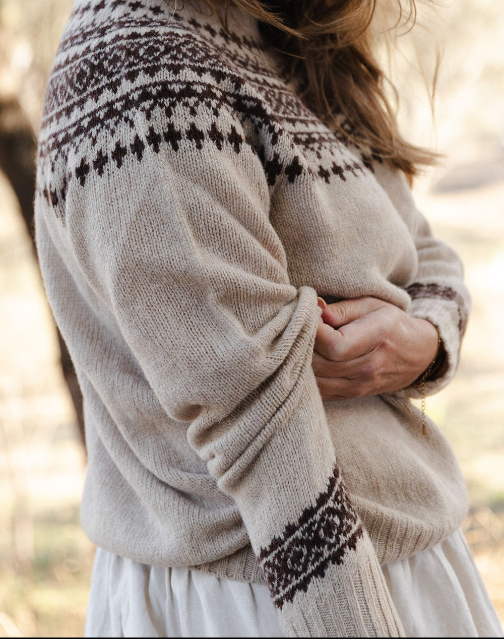 Woman wearing a beige fair isle knit sweater with brown pattern in an outdoor setting