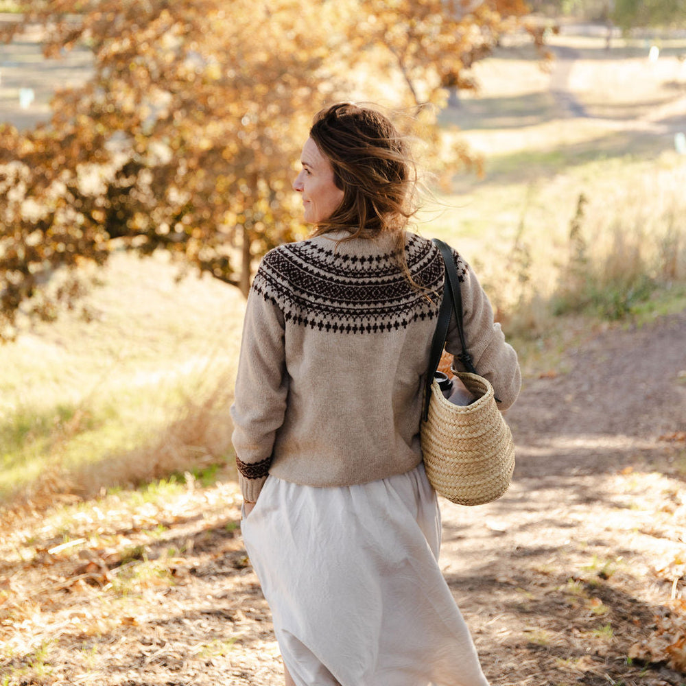 Woman walking along a path in a fair isle knit sweater in a park with autumn foliage