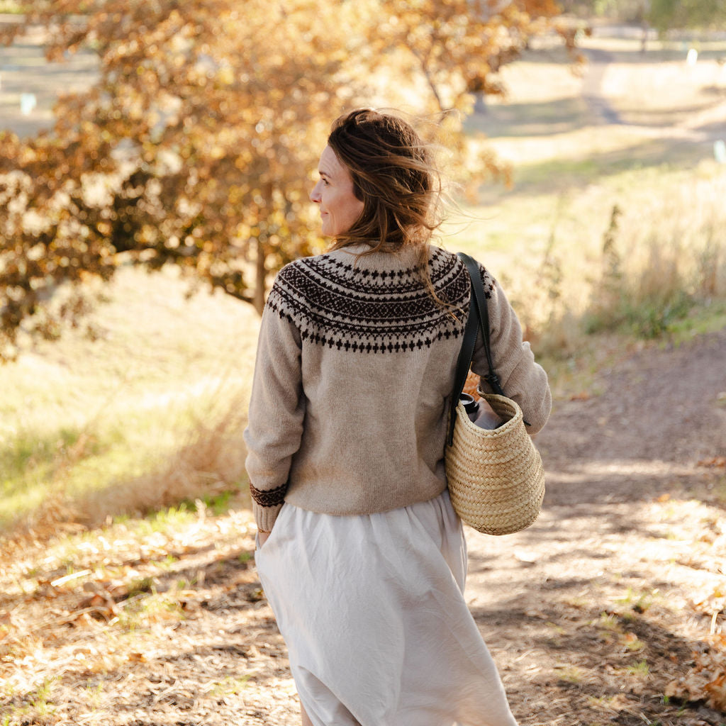 Woman walking along a path in a fair isle knit sweater in a park with autumn foliage