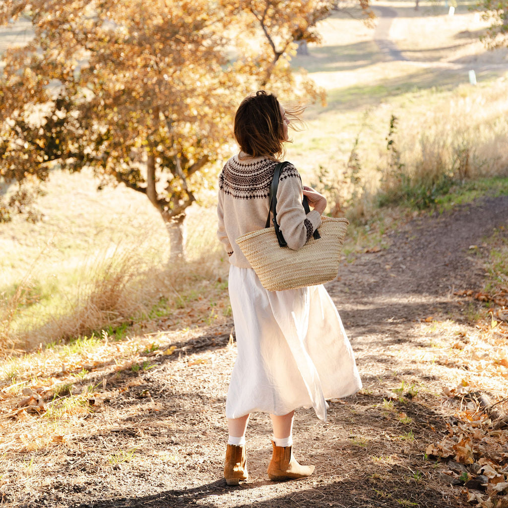 Woman walking along a path in a fair isle knit sweater in a park with autumn foliage