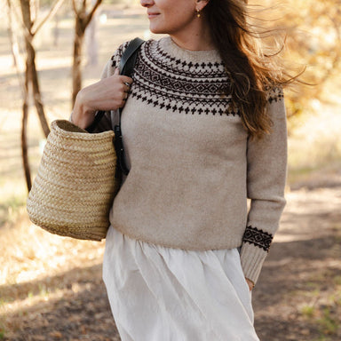 Woman wearing a fair isle knit sweater and holding a woven bag outdoors.