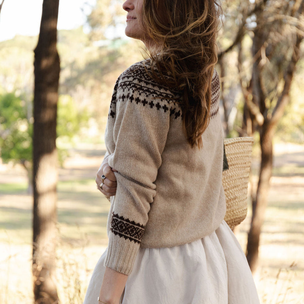 Woman wearing a fair isle knit sweater and white skirt in a forest setting