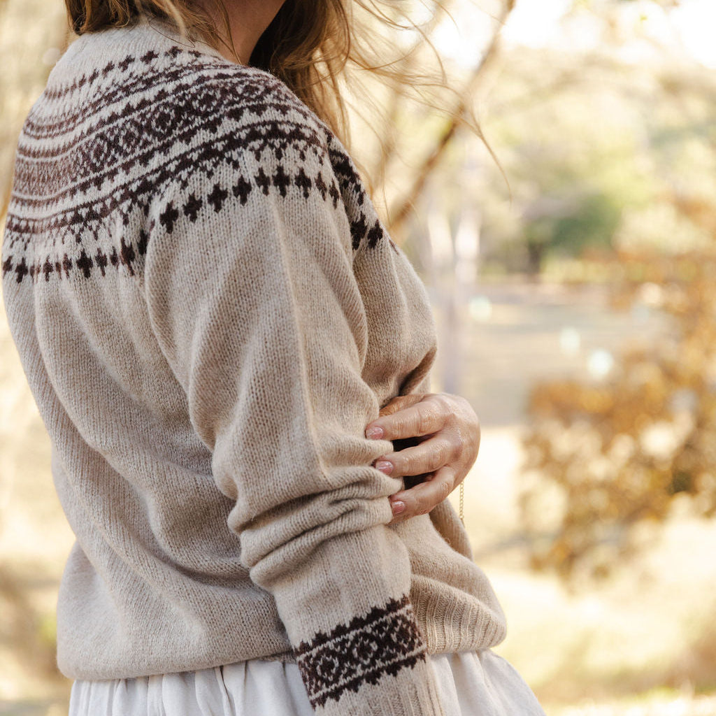 Person wearing a beige fair isle knit sweater with brown pattern in an outdoor setting