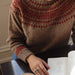 Person wearing a patterned sweater with a cup of coffee and an open book on a table.
