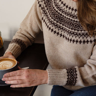 Person wearing a fair isle knit sweater holding a cup of coffee.