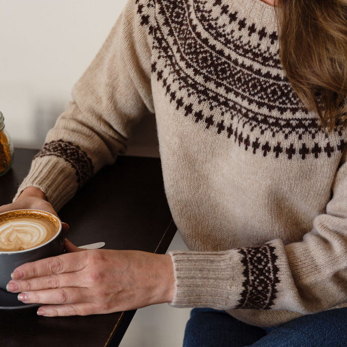 Person wearing a fair isle knit sweater holding a cup of coffee.