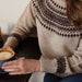 Person wearing a fair isle knit sweater holding a cup of coffee.