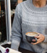 Person in a fair isle knit sweater holding a cup of coffee and a magazine outdoors