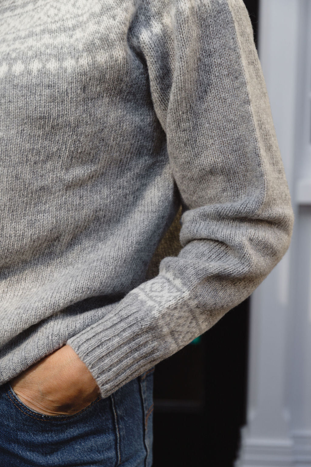 Close-up of a person wearing a grey fair isle knit sweater with a patterned design.