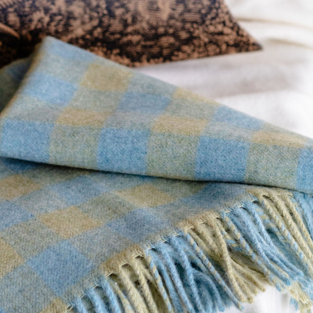 Checkered blanket with fringes on a bed with pillow shaped box packaging