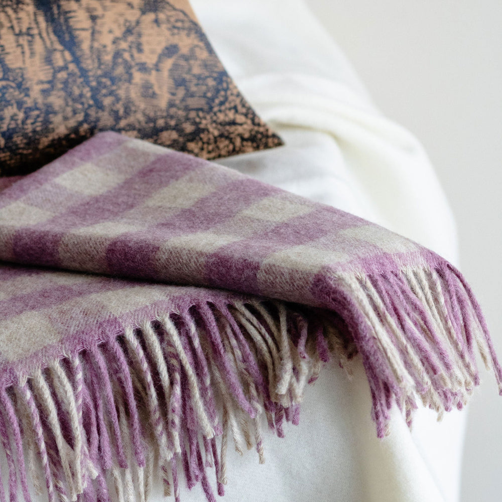 Purple checkered blanket with fringes draped over a white surface