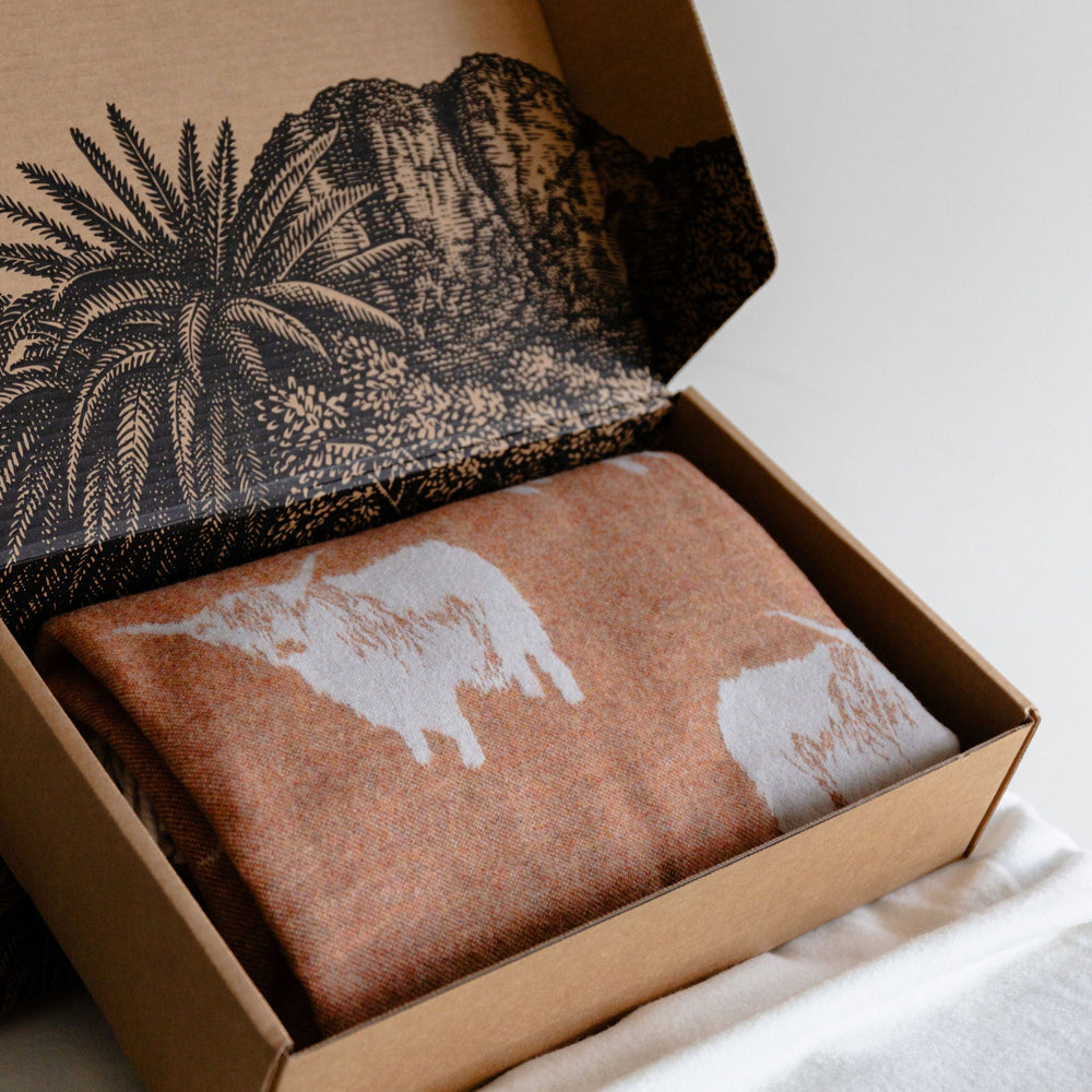 Open cardboard box with patterned fabric and brown fabric with animal print on a white surface