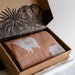 Open cardboard box with patterned fabric and brown fabric with animal print on a white surface