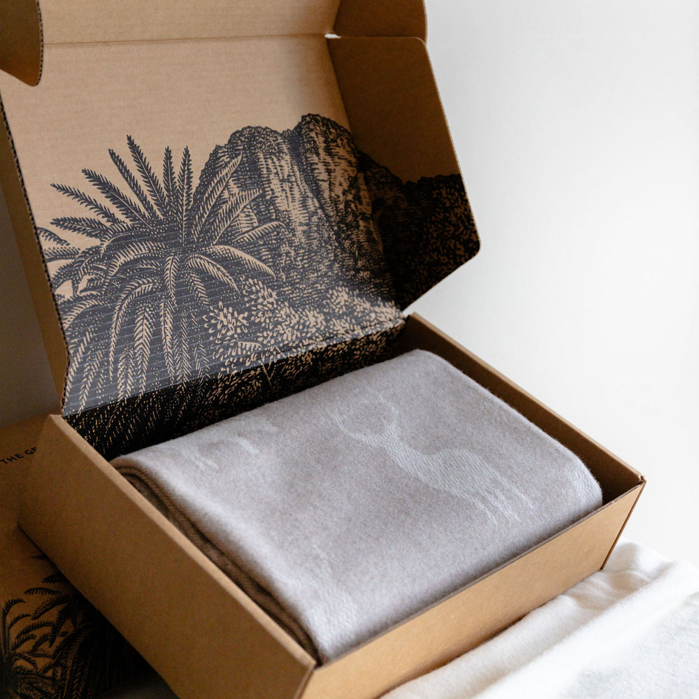 Open cardboard box with a textured interior, containing a gray fabric item on a white surface.