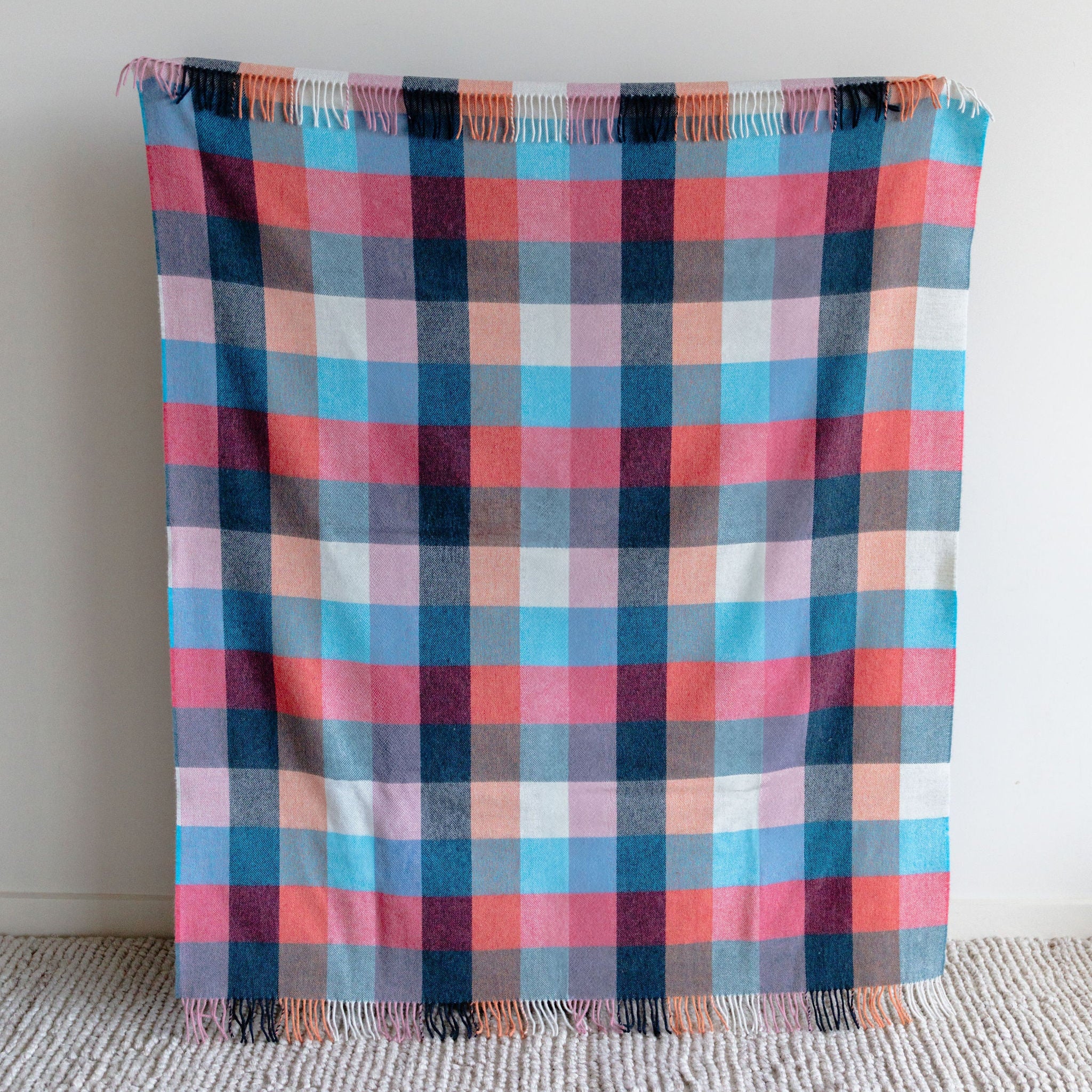 Plaid blanket with pink, blue, and black pattern on a light gray background