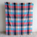 Plaid blanket with pink, blue, and black pattern on a light gray background