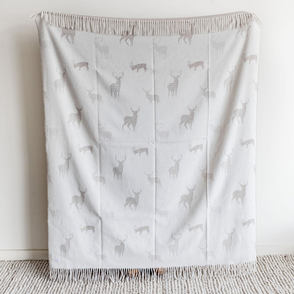 Gray blanket with deer pattern draped over a chair against a white wall.