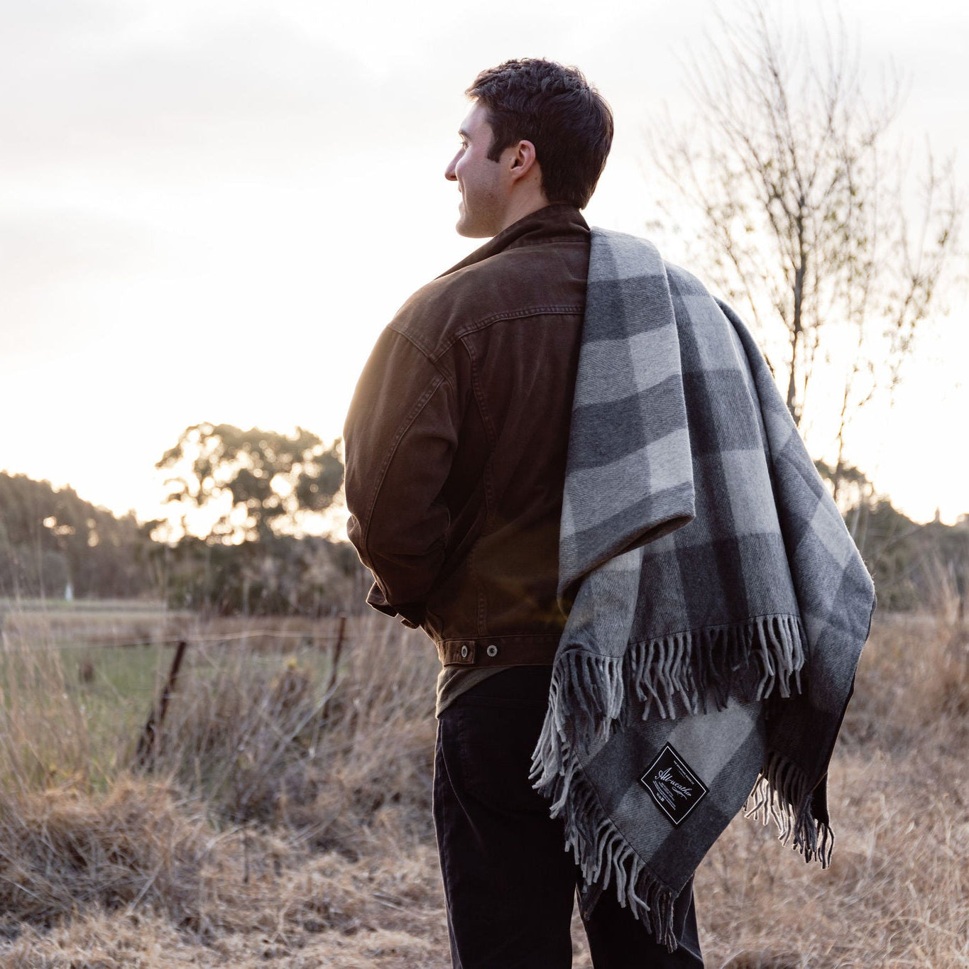 Man standing in a field with a plaid blanket draped over his shoulders