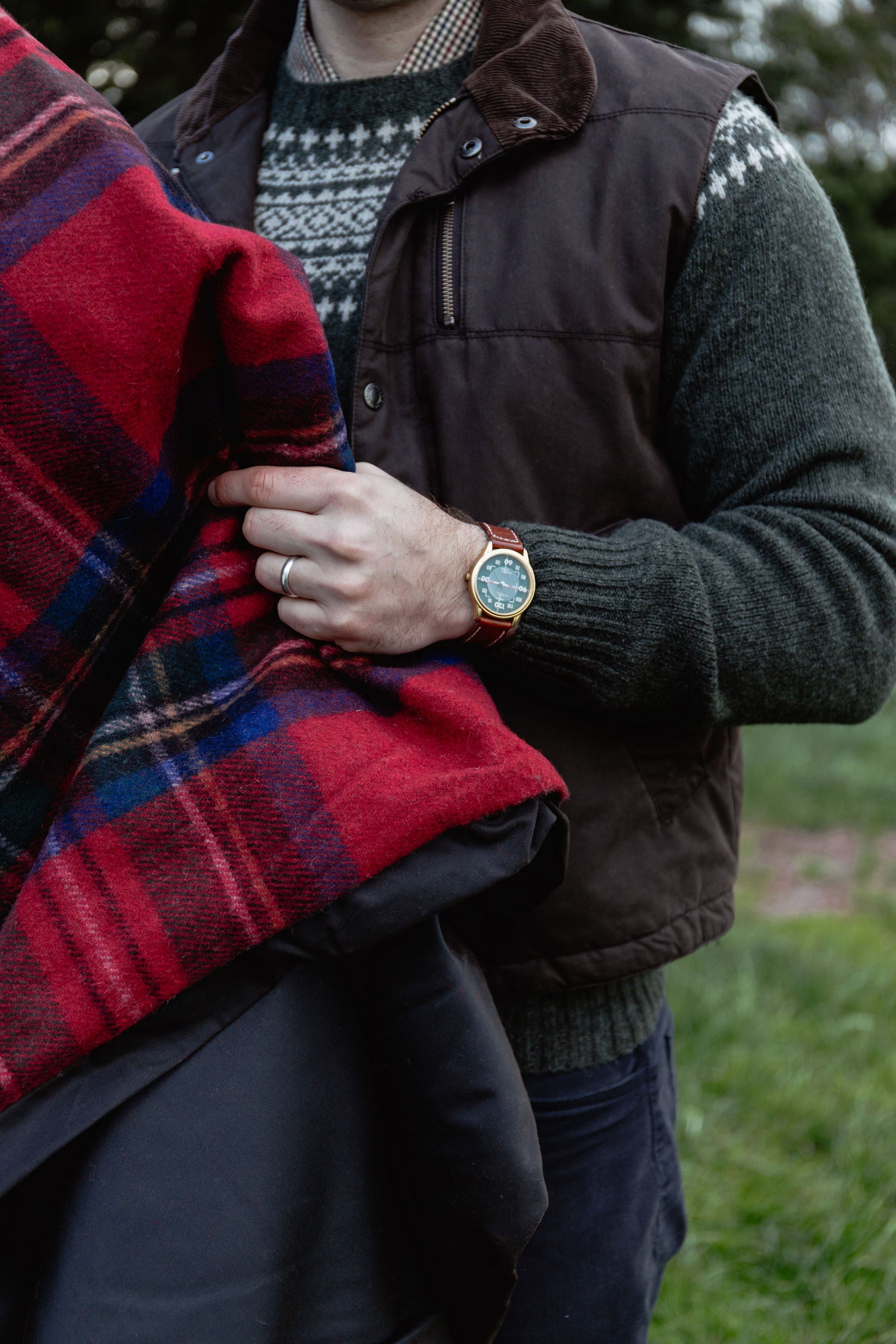 Person wearing a brown vest and holding a red plaid blanket outdoors