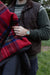 Person wearing a brown vest and holding a red plaid blanket outdoors