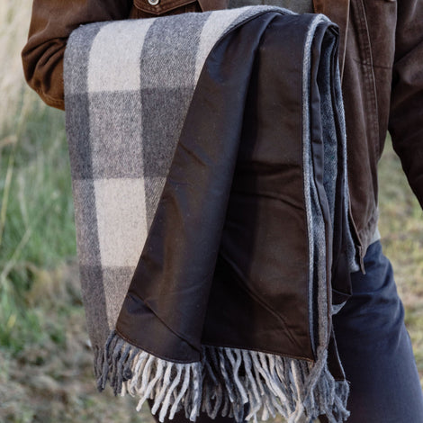 Person wearing a brown jacket with a plaid blanket draped over their shoulders in an outdoor setting.