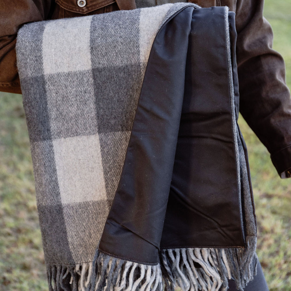 Person wearing a brown jacket with a plaid blanket draped over their shoulders outdoors.