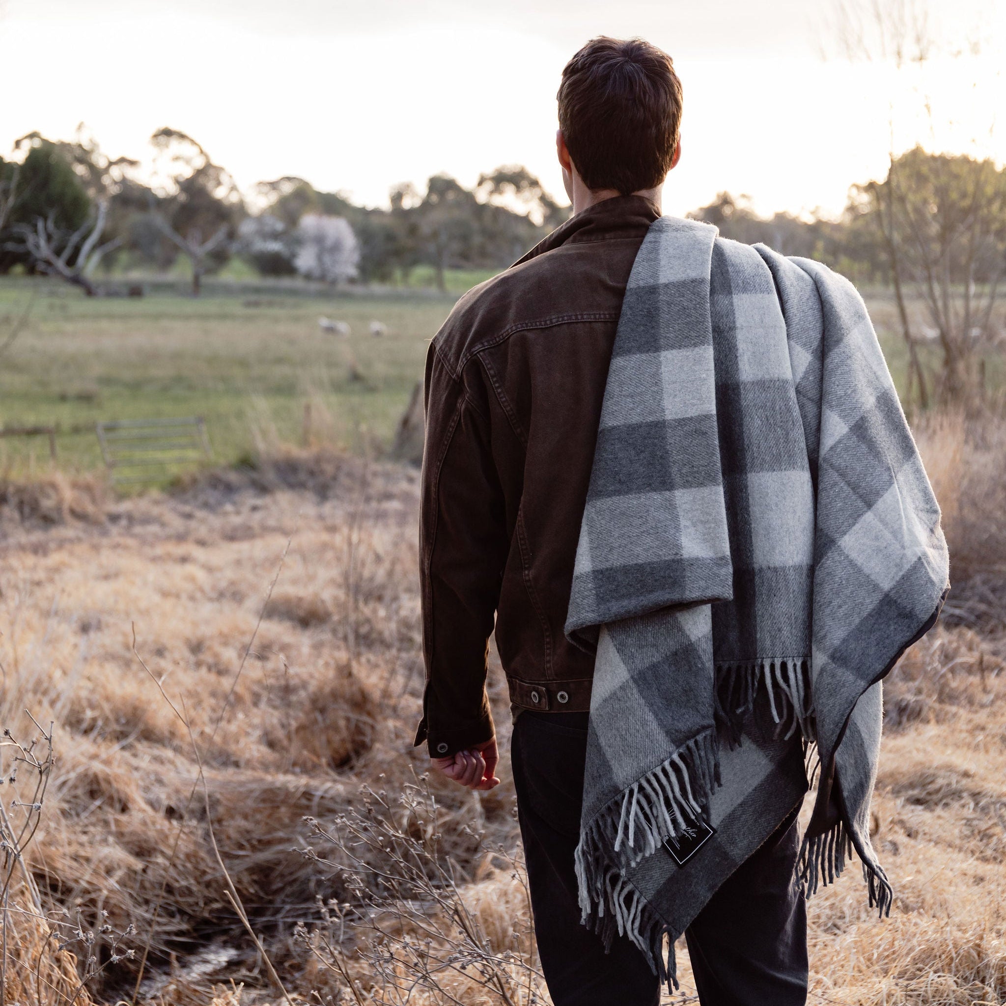 Person standing in a field with a checkered blanket draped over their shoulders