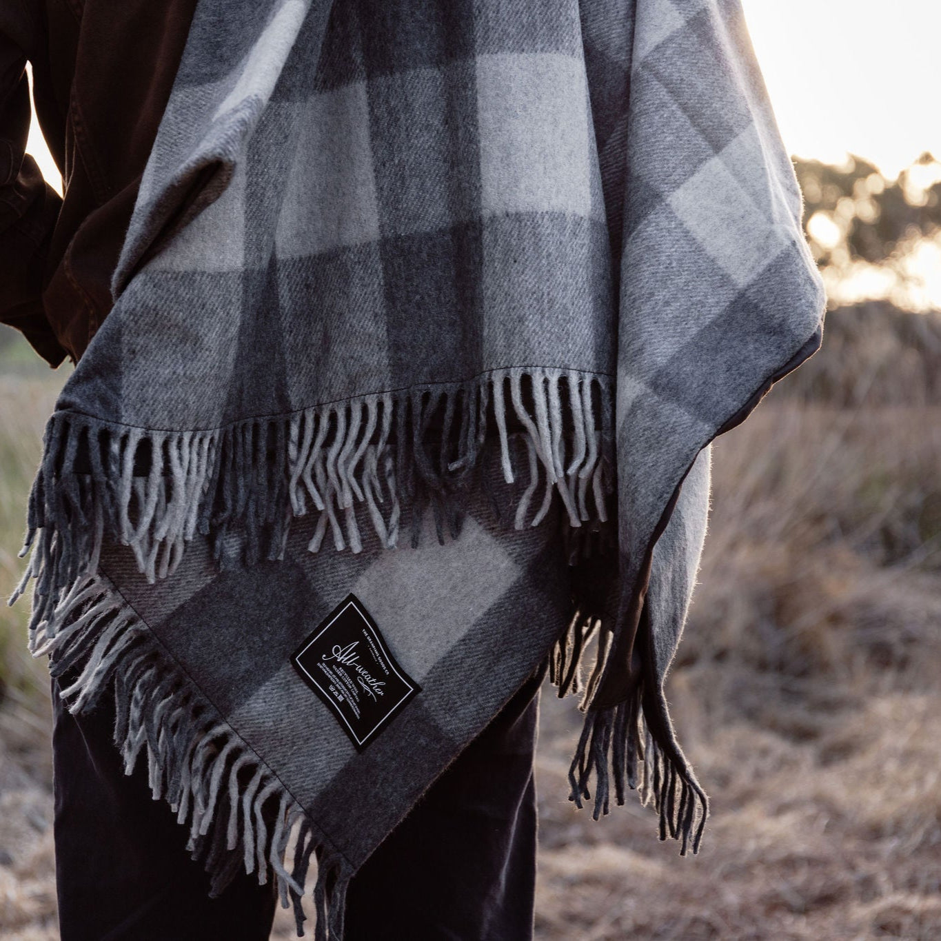 Person wearing a plaid poncho with a logo in an outdoor setting