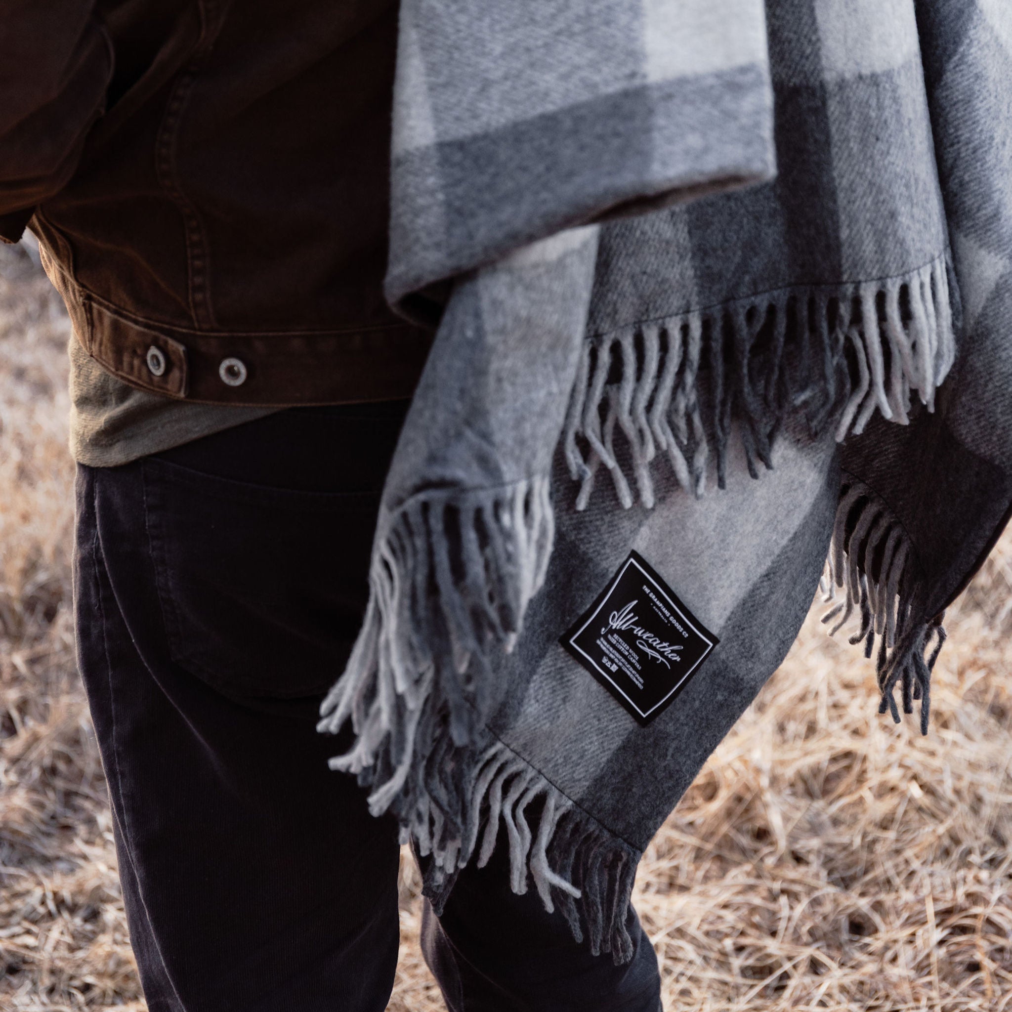 Person wearing a plaid blanket with a brand logo over their shoulders outdoors.