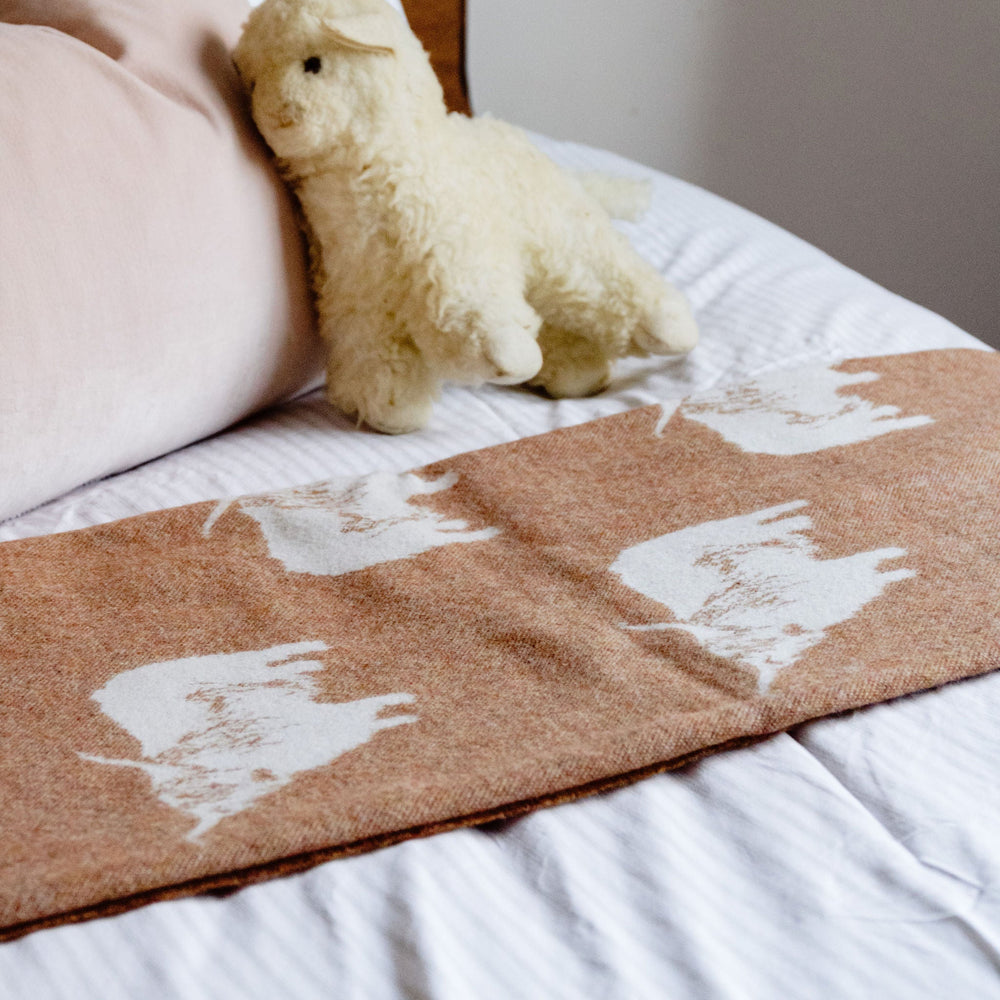 Teddy bear on a bed with a brown blanket featuring white paw prints