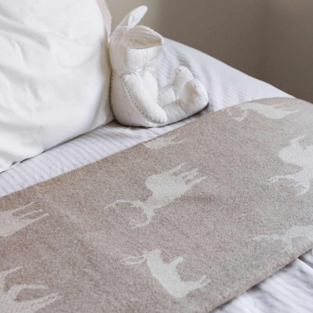 White ballet shoes on a bed with a gray blanket featuring animal prints.