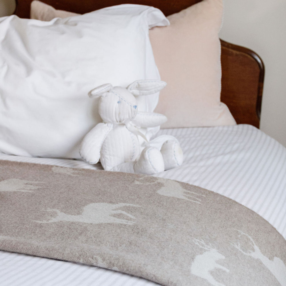 Bed with white bedding, brown headboard, and knitted white bear toy.