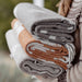 Stack of folded blankets in various colors held by a person wearing a patterned sweater.