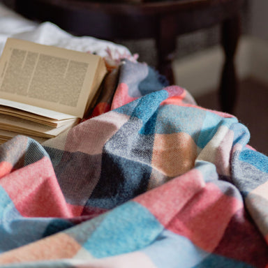 Colorful plaid blanket on a surface with a blurred background of a candle and book.