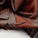 Close-up of a rust plaid fabric with fringes on a textured surface