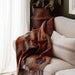 Brown plaid blanket draped over a beige sofa with a plant in the background