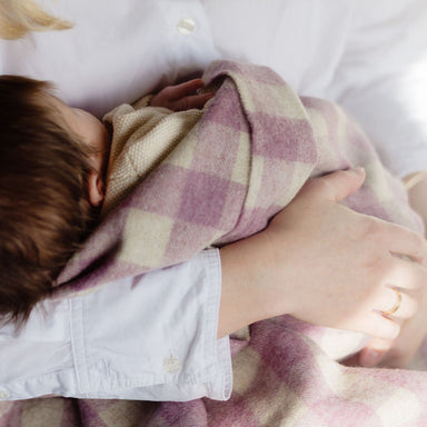 Baby wrapped in a pink and white checkered blanket, held in a mother's arms.